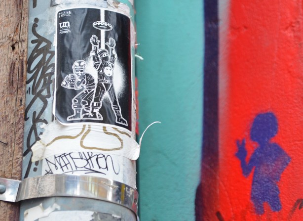 urban ninja squadron sticker on a pole, little figure stencil in blue on wall beside it 