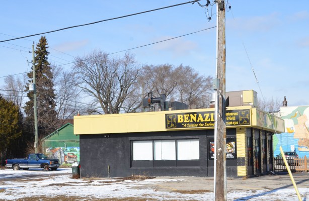 empty restaurant, benazi, on a corner lot, murals on the buildings behind it 
