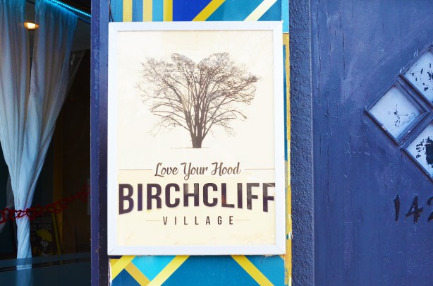 poster on the outside of a store, blue wall, picture of a tree and words that say Love your hood, Birchcliff village