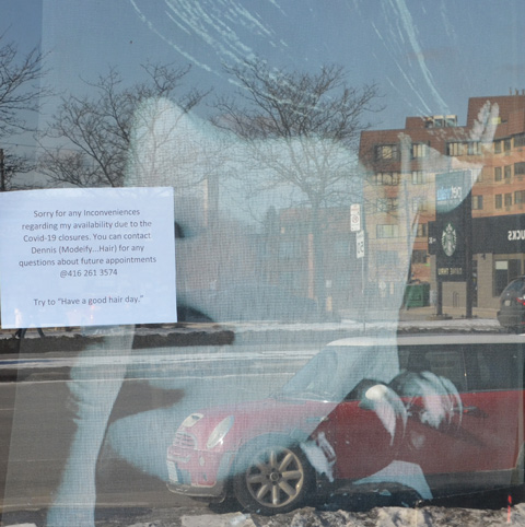 looking in a store window, a large picture of a woman looking back out, with a sign on the window re opeings and closings for covid 19 