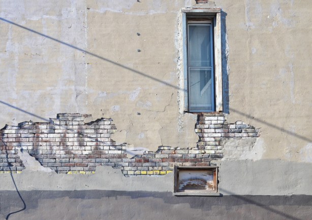 ghost sign that says groceries, under a cracking layer of concrete, on a wall with a couple of windows