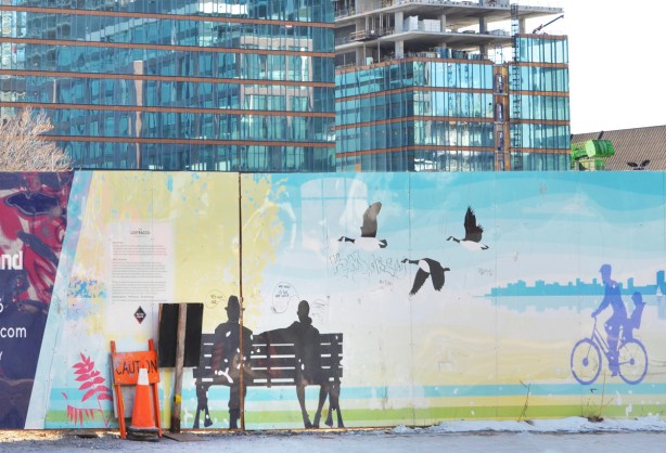 painted hoardings of a couple sitting on a bench, a child on a bike, some Canada geese, by Pam , around a construction site