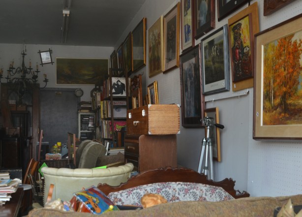 looking in the window of a junk vintage store, framed pictures on the wall, a shelf of old records, a trunk, and other stuff