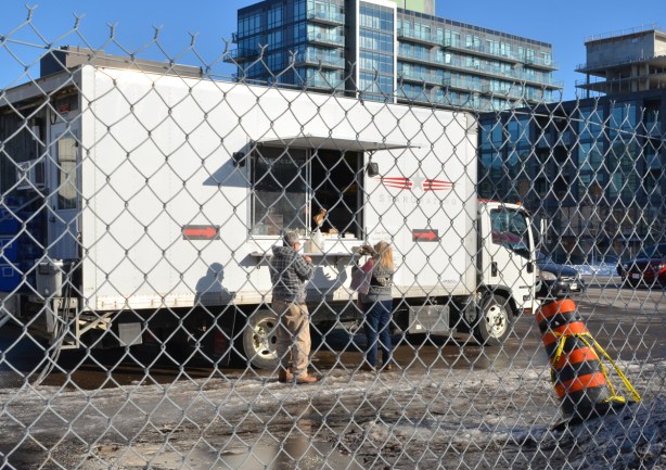 two people buying coffee and muffins from a food truck in a lot with many other white trucks 