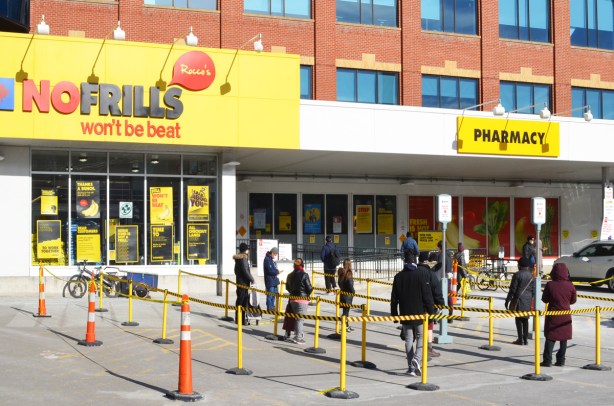people lined up waiting to get into No Frill grocery store, keeping the 2 metres apart