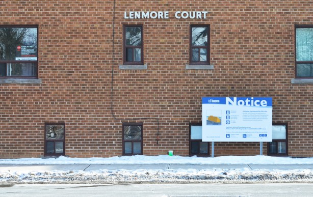 Lenmore Court, an older brick apartment complex, with a blue and white Toronto notice of development sign on it 
