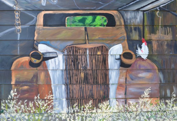 mural, front of an old rusty car with a white chicken standing on one fender 
