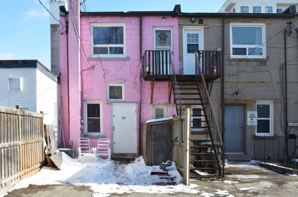 back of a store & apartment, in an alley, building is brick painted pink, stairs to upper level doors, snow on the ground