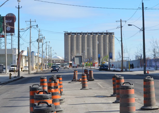 looking east on Queens Quay from Lower Sherbourne with old concrete silos in the distance, lots of orange and black traffic cones in the middle of the street in the foreground 