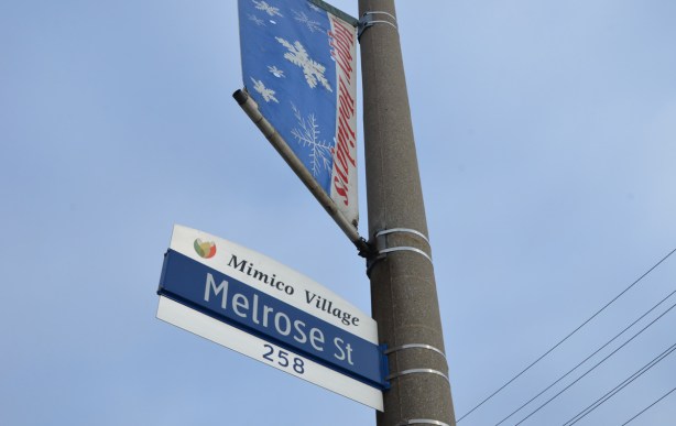 Toronto street sign for Mimico village, Melrose street,, on the same pole is a banner above it that says happy holidays 