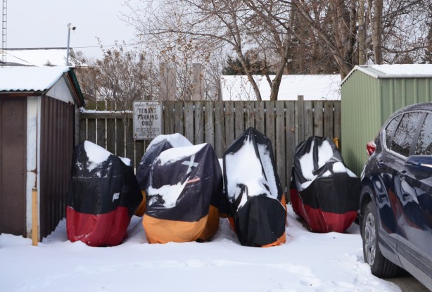 four motorcycles under individual covers and parked outside in the snow 