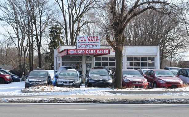 an old gas station that is now a used car dealership, with many cars parked outside in the snow 
