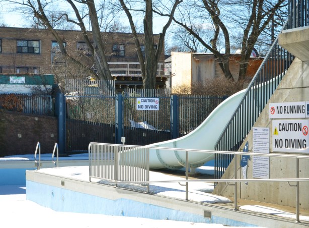 outdoor waterslide at an outdoor pool closed for the winter, sign that says no running, no diving 
