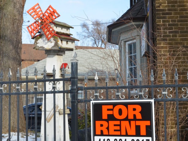 a large white bird house with a red windmill on it, behind a wrought iron fence, and a for rent sign on the fence 