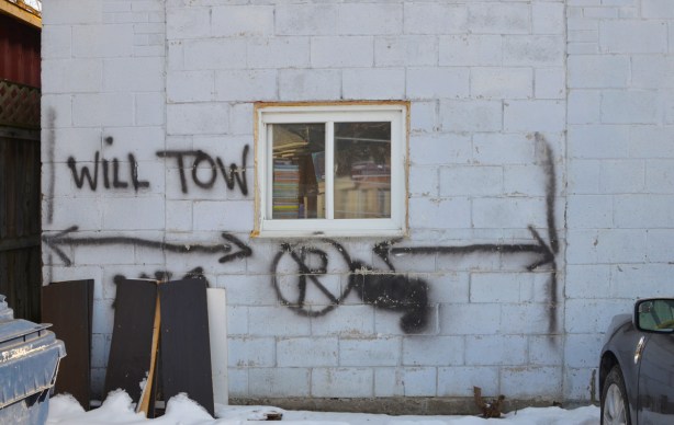 from the outside, a window in a concrete block wall, window is full of books, sign spray painted on wall that says no parking, will tow 