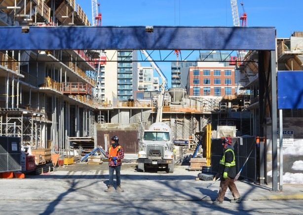 workmen by the entrance to a construction site, with concrete mixer backed into the site