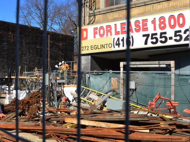 behind that metal bars of a construction barrier, workmen are consulting a paper 