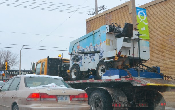 a zamboni on the back of a tow truck, travlling on a toronto street 