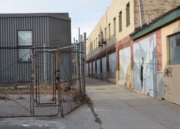 small alley with a building on the right side with panels at street level that are decorated with murals