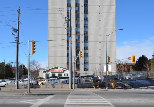 a grey apartment building in the background, a house as auto sales, cars parked in front, used car lot, 