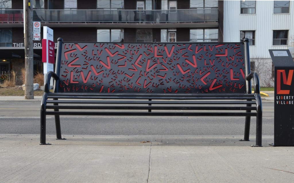 a black metal bench with cut outs in red, of L and V shapes on the back piece