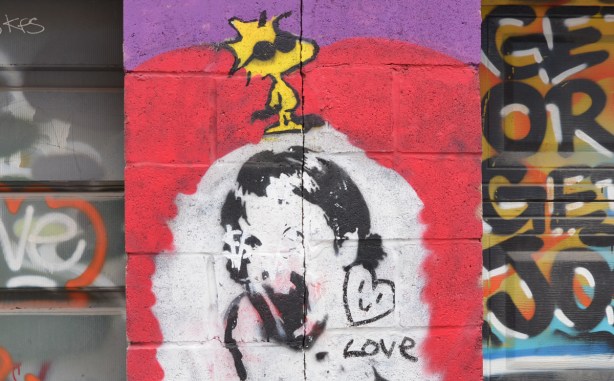 little yellow Woodstock with black sunglassses stands above a black stencil on white of a girls head, a love heart is there too 