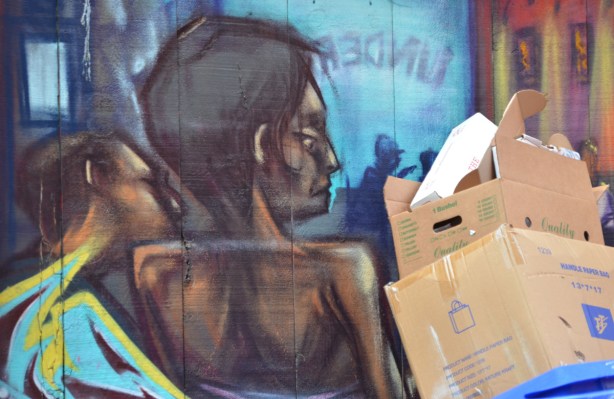 cardboard boxes stored against a wall with a mural of a woman from the back view 