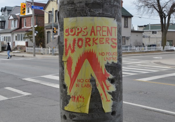 poster on a utility pole, yellow paper, orange words, Cops aren't workers,