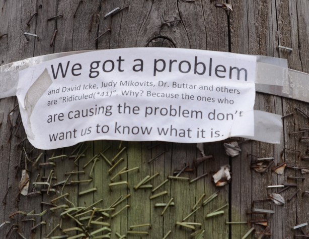ripped paper on wooden pole with lots of staples, we got a problem, a covid protest piece 