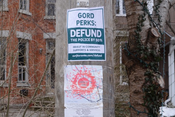 two posters on a pole, one is Gord PErks Defund the police by 50 percent and the other is Disco 3000