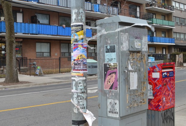 many posters on a pole and a metal box on a sidewalk