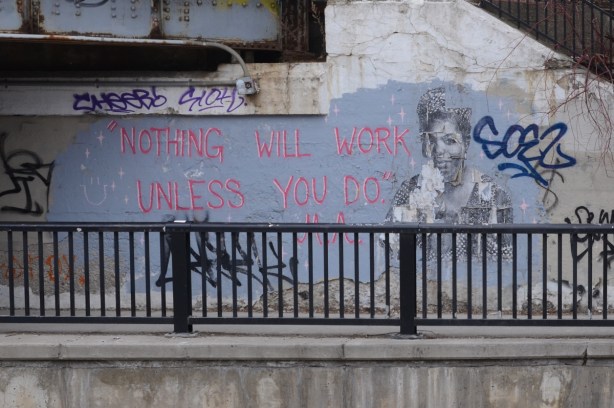 on an underpass wall, a black and white picture of a woman, Maya Angelou, and words in pink that say Nothing will work unless you do. This a quote from Maya Angelou 