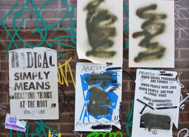 5 posters on a wall, most of the words have been blacked out. The poster that is still totally legible says Radical simply means 
