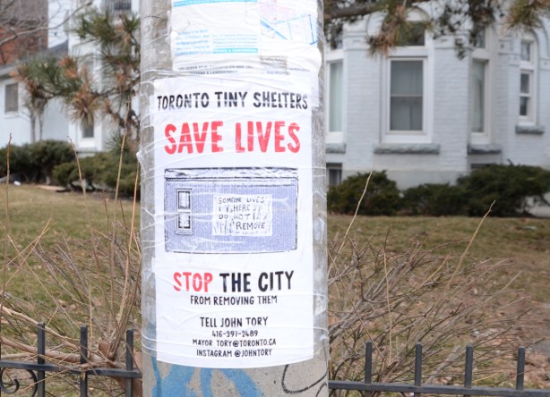 a poster on a pole that wants Toronto city hall to save lives by not tearing down tiny shelters for the homeless that a man has been making