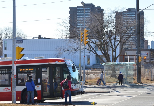 corner of Midland and Sheppard East, a Midland bus is northbound, bus shelter with 2 people across the street 