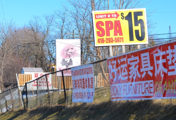 advertising signs along a fence, spa for 15 dollars, a Chinese furniture store, a pink poodle picture