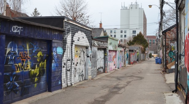 row of garages in an alley with graffiti and street art on them 