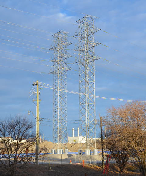 two tall metal hydro poles with lots of blue sky, power plant in the distance, and looking very small