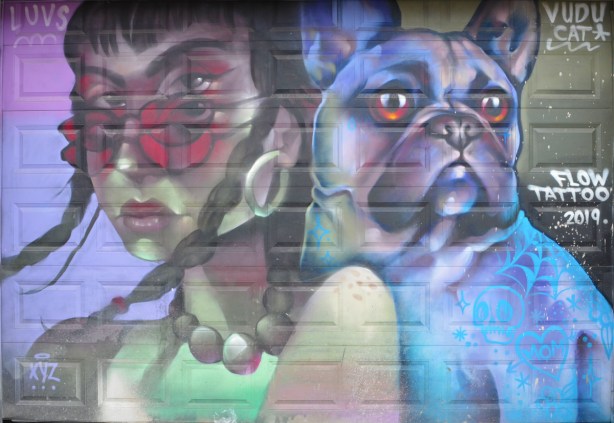 mural of a woman with large bead necklace and rose coloured sunglasses, beside of dog in shades of blue and purple, 