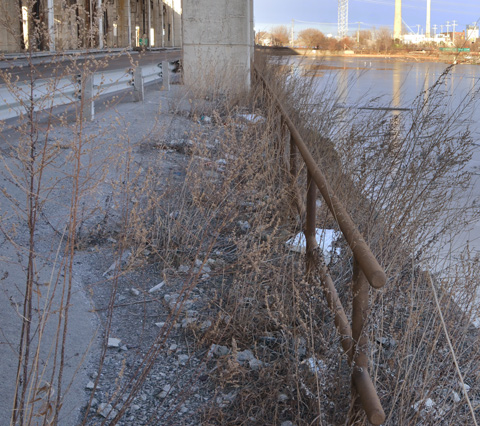 old rusty metal barrier between the Keating Channel and the road, with some weeds and gravel