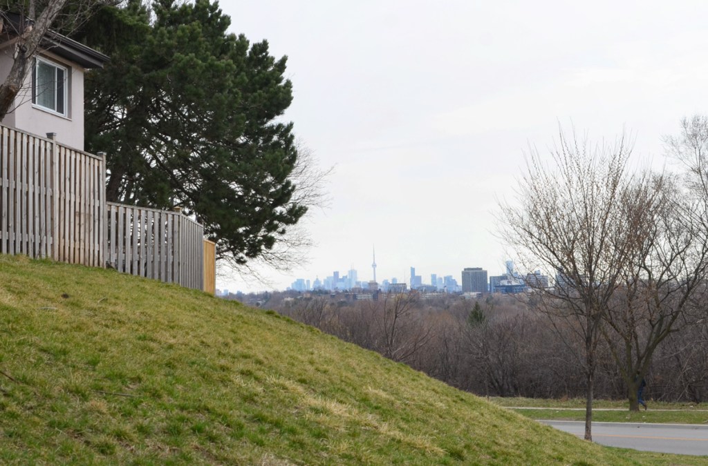 Looking beyond a fence and some houses to see the CN Tower and Toronto downtown skyline in the distance