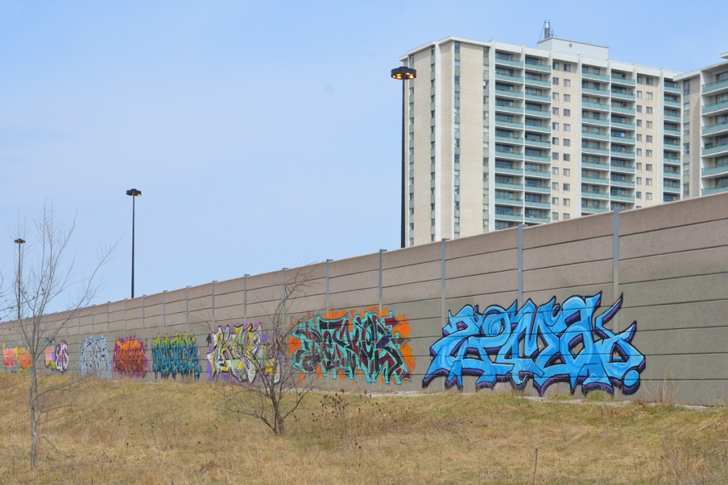 text graffiti on the concrete wall along west side of DVP, apartment building in the background, 