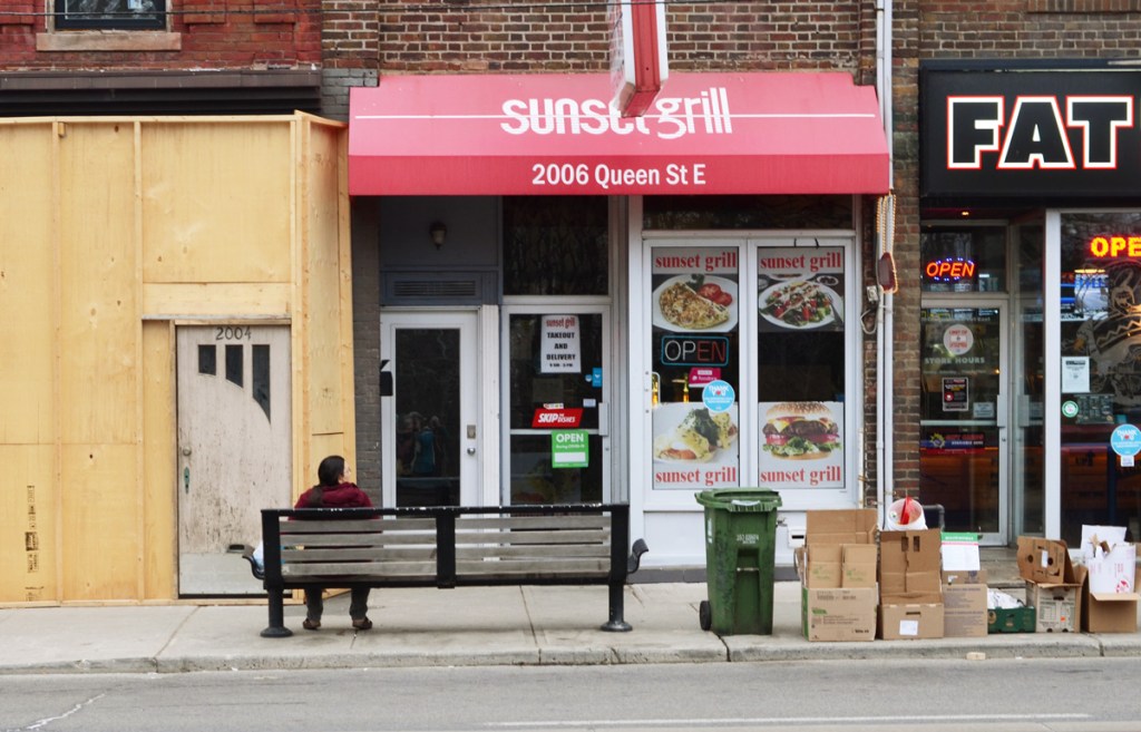 a person sits on a bench in front of the Sunrise Grill on Queen East
