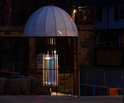 Under an umbrella shape - a series of mirrors making a cylinder that rotates, lights shining on it from the sides so the shapes of lights being reflected changes as the cylinder moves