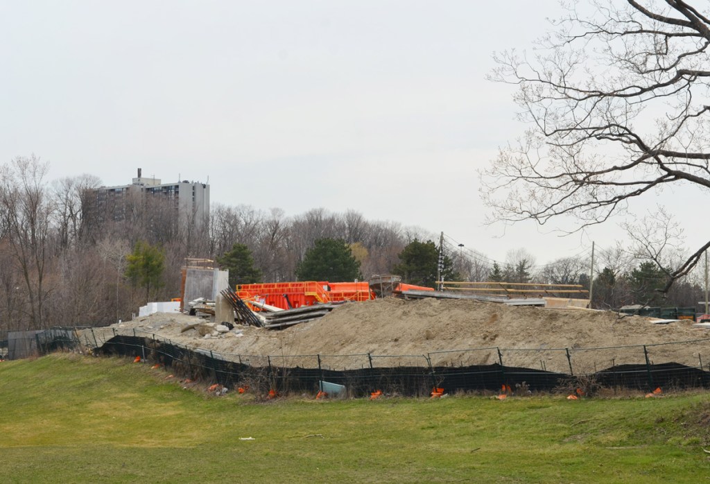 fence around a pile of dirt, construction site, with orange objects, apartment building in the background