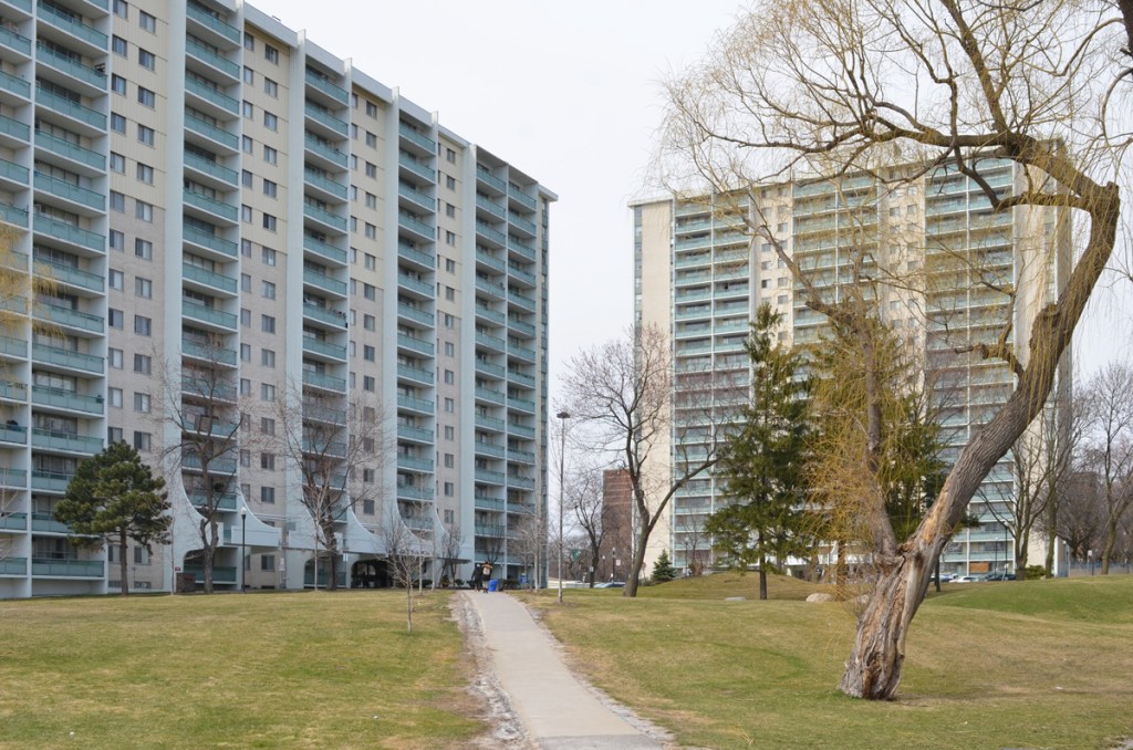 A path crosses a large lawn in front of two apartment buildings