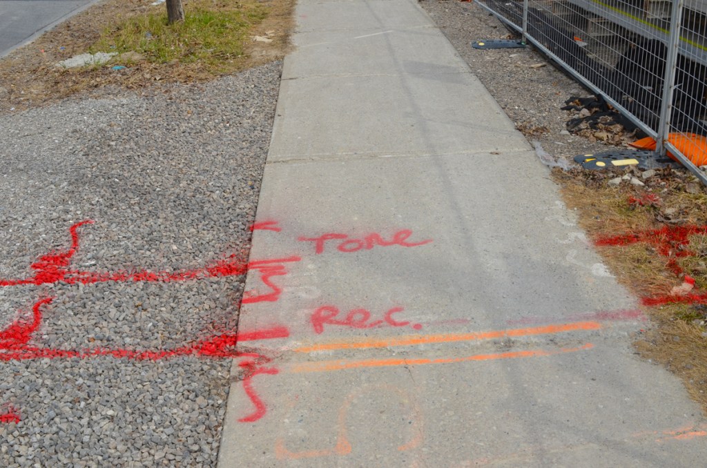 red and orange spray paint markings on a sidewalk by a construction site 