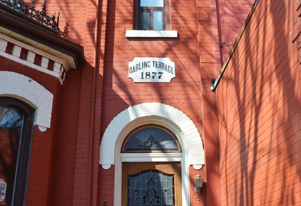 Semi circular window over the front entrance of a door in Darling Terrace, a row of orange painted houses with white trim on Parliament street in Cabbagetown