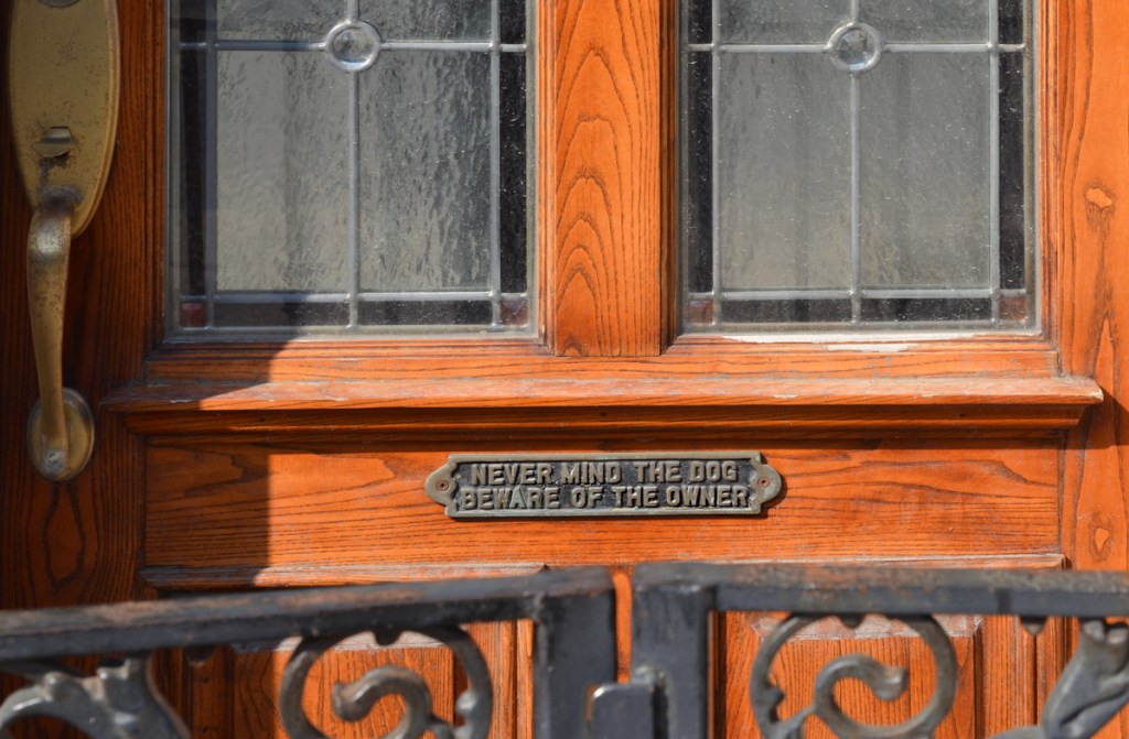 front door of a house behind a wrought iron gate with plaque on it that says Never mind the dog beware of the owner