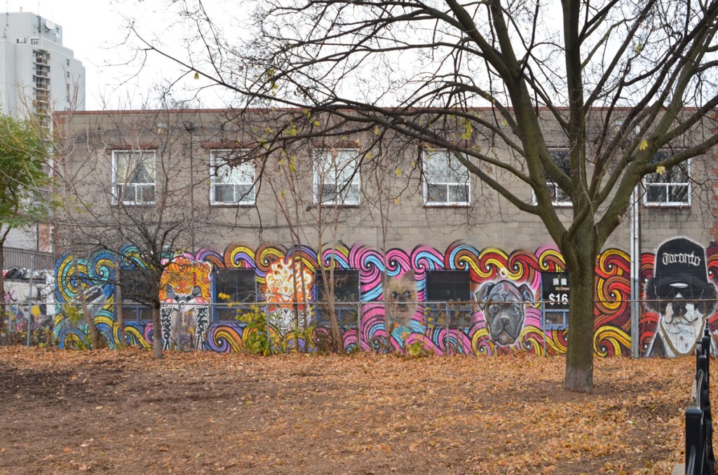 beside a park, a two storey concrete building with murals of dog portraits on the first storey, between the windows 